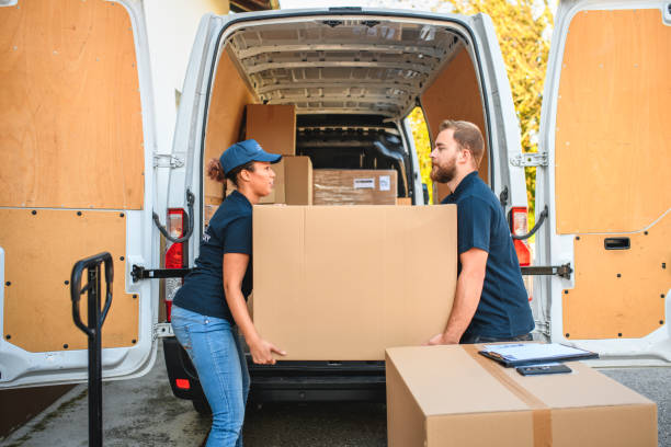 Delivery team of man and woman lifting a giant cardboard box towards the storage space of the van.
