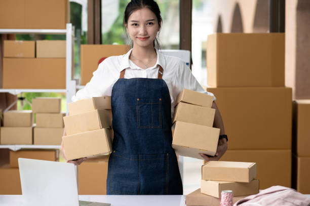 Young woman owner of online business and small courier, standing with box in office smiling proudly, parcel delivery, e-commerce.